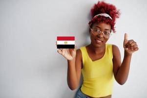 afrikanische frau mit afrohaar, trägt gelbes unterhemd und brille, hält ägypten-flagge lokalisiert auf weißem hintergrund, zeigt daumen hoch. foto