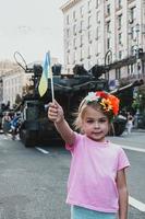 kiew, ukraine - 23. august 2022. kleines ukrainisches mädchen mit flagge in der hand posiert in der nähe des zerstörten panzers. foto