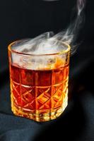 alkoholisches Getränk. Ein Cocktail mit Whiskey oder Cognac mit Feuer und Rauch aus nächster Nähe, dunkelschwarzer Hintergrund foto