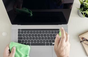 computerreinigungskonzept. Draufsicht auf eine männliche menschliche Hand, die einen Laptop-Bildschirm mit Reinigungsspray und antistatischem Tuch reinigt foto