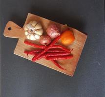 Zutaten für Knoblauch, Schalotte, Chili und Tomaten auf einem Holzbrett mit schwarzem Hintergrund foto