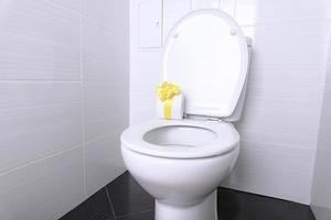 Weiße Haustoilette mit Spülung und weißes Toilettenpapier mit einer gelben Geschenkschleife im Badezimmer. Quarantänekonzept. foto