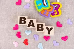 Holzblöcke mit dem Wort Baby und kleinen bunten Herzen darunter. Sicht von oben foto
