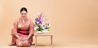 Junge asiatische Japanerin aus den 20ern trägt traditionellen Kimono, macht Ikebana-Blumenarrangement foto