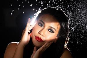 indische gebräunte haut asiatische frau zeigt gesichts-make-up mit hintergrundbeleuchtetem licht und wasserspritzerspray