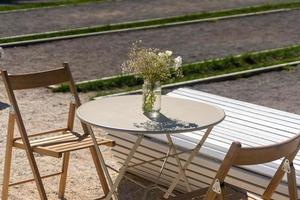 Straßencafe. Holzstühle und runder Metalltisch mit Blumenstrauß an einem sonnigen Tag. foto