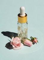 Flasche 24 Karat Goldserum auf blauem Hintergrund mit Rosenblüten. das konzept der hautpflege zu hause. foto