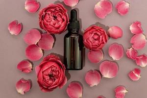Hausgemachtes Hautpflegeprodukt aus ätherischem Rosenöl auf rosafarbenem Hintergrund aus Rosenblättern in kosmetischer dunkler Glasflasche mit Tropfer zur Befeuchtung der Haut. markenloses Paketmodell foto