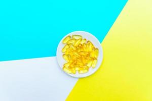 Draufsicht auf Omega-3-Fischöl-Gel-Casules auf weißem Teller auf weißem, blauem und gelbem Hintergrund. kreatives Gesundheitskonzept foto