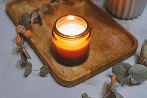 Etikettenmodell des Glasgefäßes mit handgefertigter Kerze auf dem mit Eukalyptuszweigen verzierten Holztablett. aromatischer gemütlicher lebensstil foto