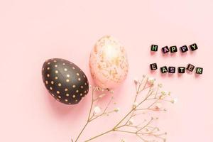 Bemalte Holzeier in Gold-, Schwarz- und Rosenfarben mit Gypsophila-Zweig auf rosa Hintergrund. frohe ostern text mde aus schwarzen perlen foto