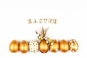 ostern festliche dekoration. Blick von oben auf die mit goldener Farbe gefärbten Ostereier und Inschrift auf Englisch frohe Ostern. Holzbuchstaben auf weißem Hintergrund. verschiedenes gepunktetes Design foto