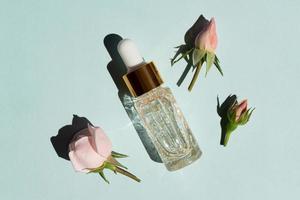 Flasche 24 Karat Goldserum auf blauem Hintergrund mit Rosenblüten. das konzept der hautpflege zu hause. foto