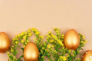 Festliche Wohnung mit goldenen Ostereiern und Solidago-Blumen auf braunem Hintergrund mit Kopierraum foto