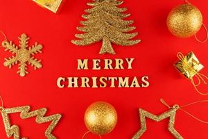 festliche grußkarte. frohe weihnachten schriftzug auf rotem papier mit goldenen glitzernden spielzeugen. foto