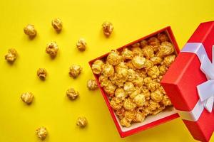 Rote Geschenkbox mit weißer Schleife voller leckerem Karamell-Popcorn auf gelbem Hintergrund. foto