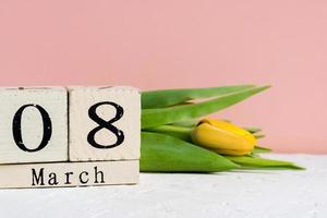 Internationaler Frauentag. Holzkalender 8. März und gelbe Tulpen auf rosa Hintergrund foto