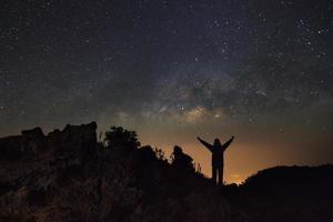 milchstraßengalaxie und silhouette eines stehenden glücklichen mannes bei doi luang chiang dao mit thailändischen spitzenzeichen. Foto mit Langzeitbelichtung. Mit Körnung