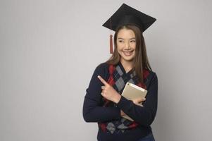 junge lächelnde frau, die abschlusshut, bildung und universitätskonzept hält foto