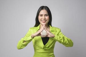 junge schöne Frau, die kleines Musterhaus über weißem Hintergrundstudio hält foto