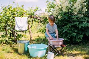 Kleines Vorschulmädchen hilft beim Waschen. Kind wäscht Kleidung im Garten foto