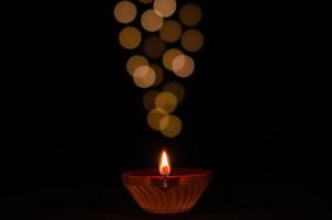 selektiver fokus auf flamme der lehm-diya-lampe, die auf dunklem hintergrund mit bokeh-lichtern beleuchtet wird. diwali-festkonzept.