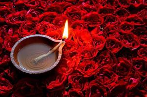 dekorative rote rosenblume rangoli für das diwali-fest mit lehm-diya-lampe, die mit flamme beleuchtet wird. foto