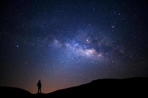 landschaft mit milchstraße, nachthimmel mit sternen und silhouette des mannes, der auf einem hohen berg steht foto