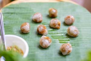 saku sai moo thailändischer traditioneller snack, der dampfenden mehlball um schweinefleisch herum mit chili isst. sie sind auf bananenblatt auf holztisch in der gartenumgebung. foto