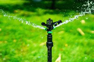 Frischwasserspritzer von der Sprinklerstange setzen sich im Grasfeld im Garten im Freien ab. foto