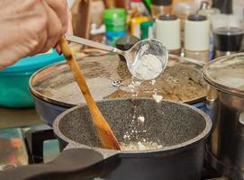 Der Küchenchef wirft Mehl in einen Topf mit Bechamelsauce, die auf einem Gasherd zubereitet wird foto