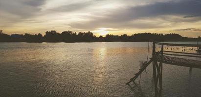 Silhouette der hölzernen Uferpromenade, Ufergegend oder Brücke mit Fluss- und Baumhintergrund bei Sonnenuntergang oder Sonnenschein. schönes natur- und freiheitskonzept. natürliche tapete mit kopierraum. foto