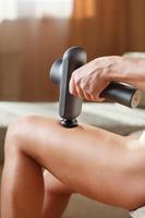 Massage von Frauenbeinen mit einem Stoßmassagegerät. foto