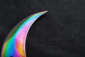 Die gebogene, scharfe Klinge des Kerambit-Dolches ist eine Regenbogenfarbe mit Farbverlauf auf dunklem Hintergrund. foto