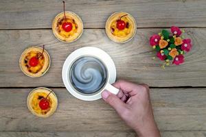 Hand hält Kaffeetasse mit Eierkuchen auf Holztisch, Ansicht von oben foto