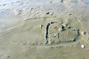 herzförmige Zeichnung auf Strandsand mit Seesternen foto