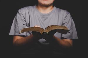 Nahaufnahme einer christlichen Frau, die die heilige Bibel hält, beten und anbeten, um Gott in der Kirche mit schwarzem Hintergrund zu danken, erwachsene weibliche Person liest Buch, foto