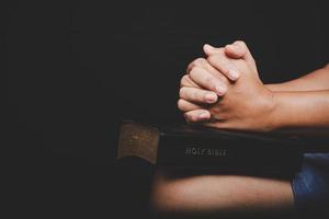Nahaufnahme der Hand der christlichen Frau auf der Heiligen Bibel sind Gebet und Anbetung für Gott sei Dank in der Kirche mit schwarzem Hintergrund, Konzept für Glauben, Spiritualität und Religion foto