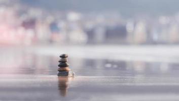 Zen-ähnliches Konzept, Kieselturmfelsen, die am Meer auf Strandsand mit verschwommenem Hintergrund übereinander gestapelt sind, Steinpyramide symbolisiert, Stabilität, Harmonie, Gleichgewicht mit geringer Schärfentiefe. foto