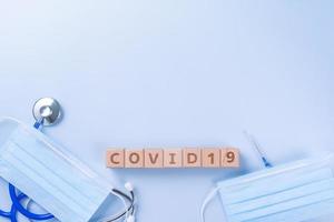 covid-19 wort holzwürfel mit maske, medizinische ausrüstung, weltkrankheit pandemische infektions- und präventionskonzept, draufsicht, flache lage, überkopfdesign foto