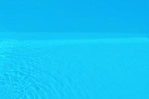 defocus verschwommene, transparente, blaue, klare, ruhige wasseroberflächenstruktur mit spritzern und blasen. trendiger abstrakter naturhintergrund. wasserwelle im sonnenlicht mit kopierraum. blaues aquarell glänzt. foto