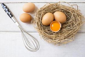 frische Bio-Eier auf Nest mit Schneebesen auf weißem Holzhintergrund. foto