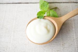 weißer joghurt mit minzblatt auf holzlöffel auf weißem holzhintergrund. draufsicht. foto