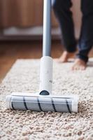 Ein Akku-Staubsauger reinigt den Teppich im Wohnzimmer mit der Unterseite der Beine. foto