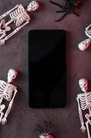 Skelette um ein Smartphone mit weißem Display auf dunklem Hintergrund. foto