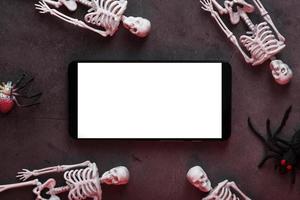 dekorative skelette liegen in der nähe des smartphones auf dunklem hintergrund. foto