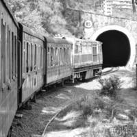 spielzeugeisenbahn, die sich am berghang bewegt, schöne aussicht, eine seite des berges, eine seite des tals, die auf der eisenbahn zum hügel fährt, inmitten grüner naturwälder. spielzeugeisenbahn von kalka nach shimla in indien-schwarz und weiß foto