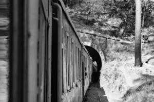 spielzeugeisenbahn, die sich am berghang bewegt, schöne aussicht, eine seite des berges, eine seite des tals, die auf der eisenbahn zum hügel fährt, inmitten grüner naturwälder. spielzeugeisenbahn von kalka nach shimla in indien-schwarz und weiß foto