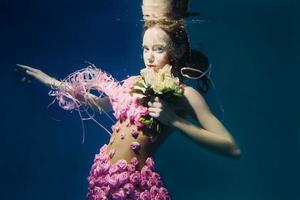 junges rothaariges Mädchen im Kleid aus Rosen unter Wasser foto