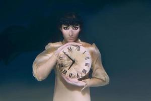 gruselige Frau mit Uhr in ihren Händen im schwarzen Schleier unter Wasser foto